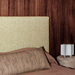 Bedroom scene with dark wood paneled wall, tan and white zebra headboard, clay colored bedding and an upholstered ottoman with white sculputral lamp