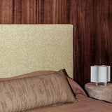 Bedroom scene with dark wood paneled wall, tan and white zebra headboard, clay colored bedding and an upholstered ottoman with white sculputral lamp