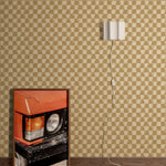 Styled interior vignette with a framed photo of a close up on an orange retro car, dark wood floors, white wall sconce with cord trailing out of the frame with a tan and beige checkerboard wallpaper backdrop.