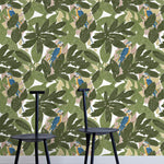 Two minimalist black chairs stand in front of a wall papered in a botanical and parrot print in green, blue and yellow.
