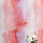 A vase of flowers stands in front of a wall papered in an abstract curvilinear pattern in mottled pink, red and purple.