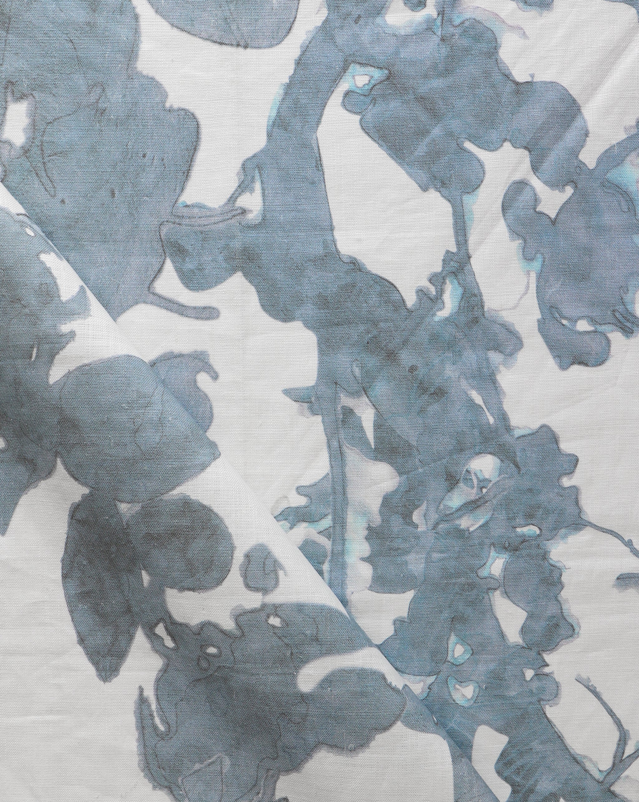 Draped fabric yardage in a watercolor tree print in blue and turquoise on a cream field.