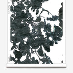 Partially unrolled wallpaper yardage in a watercolor floral print in mottled charcoal and blue on a white field.