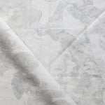 Draped fabric yardage in a watercolor tree print in shades of gray on a cream field.