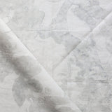 Draped fabric yardage in a watercolor tree print in shades of gray on a cream field.