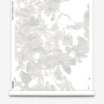 Partially unrolled wallpaper yardage in a watercolor floral print in mottled cream and gray on a white field.