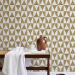 A bench with a towel and clay vases stands in front of a wall papered in a curvilinear grid print in mustard and white.