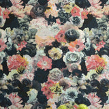 A vase of flowers stands in front of a wall covered in a dense photorealistic floral print in pink and green on a navy field.