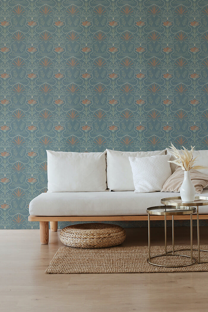 A couch and wooden end table stand in front of a wall papered in an intricate floral lattice print in green, coral and blue.
