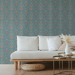 A couch and wooden end table stand in front of a wall papered in an intricate floral lattice print in green, coral and blue.