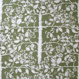 Detail of fabric in a large-scale tree and leaf print in white on a green field.