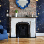 A maximalist living tableau with a fireplace and accent walls papered in a playful koi pond print in navy, gold and black.