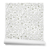 A hanging roll of wallpaper in a large-scale minimal floral print in shades of tan and gray on a white background.