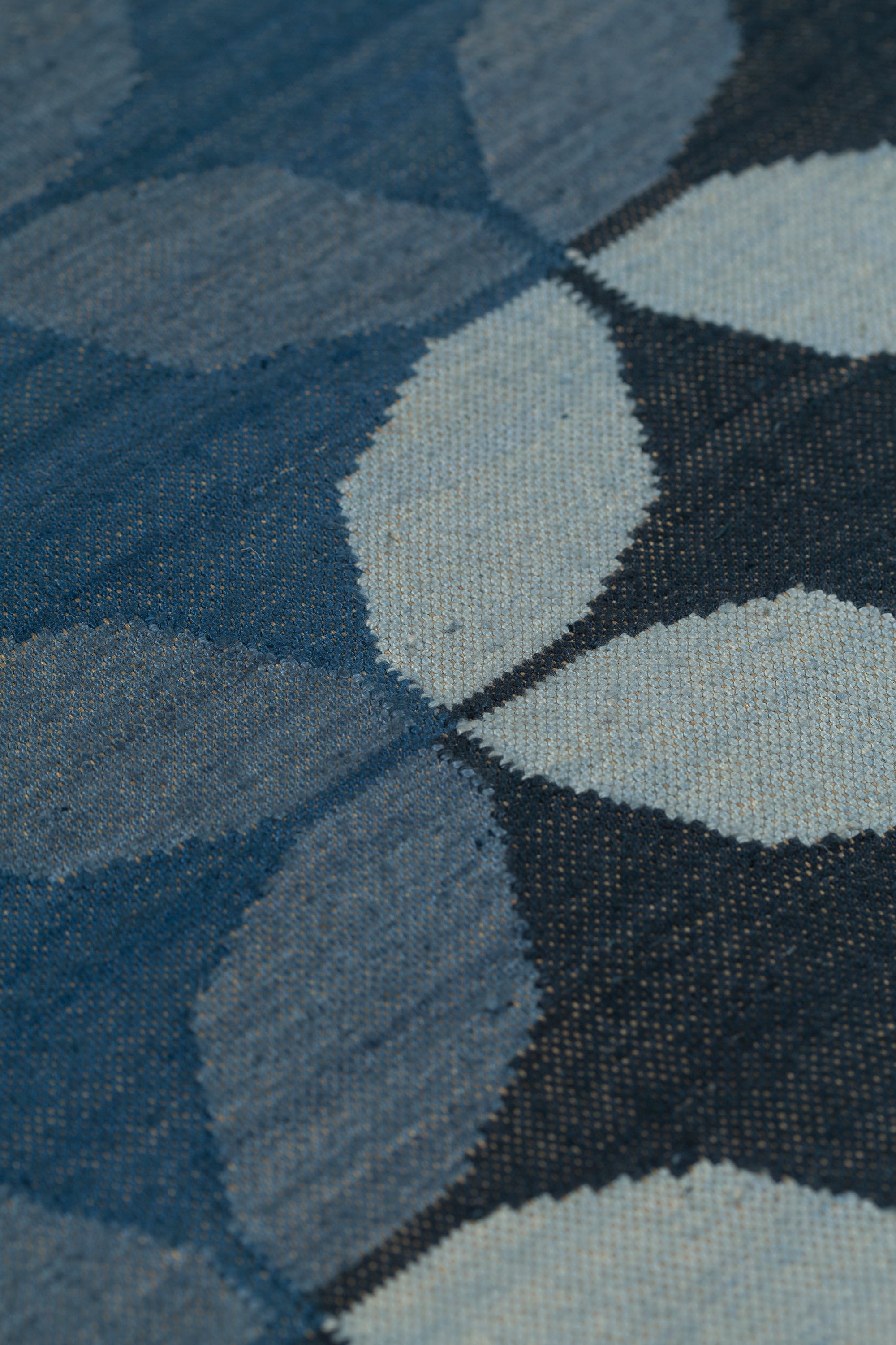 Detail of Alhambra Rug featuring a pattern of linked circles that create a star like lattice in a range of blue shades, from pale blue to chambray, indigo, to dark navy