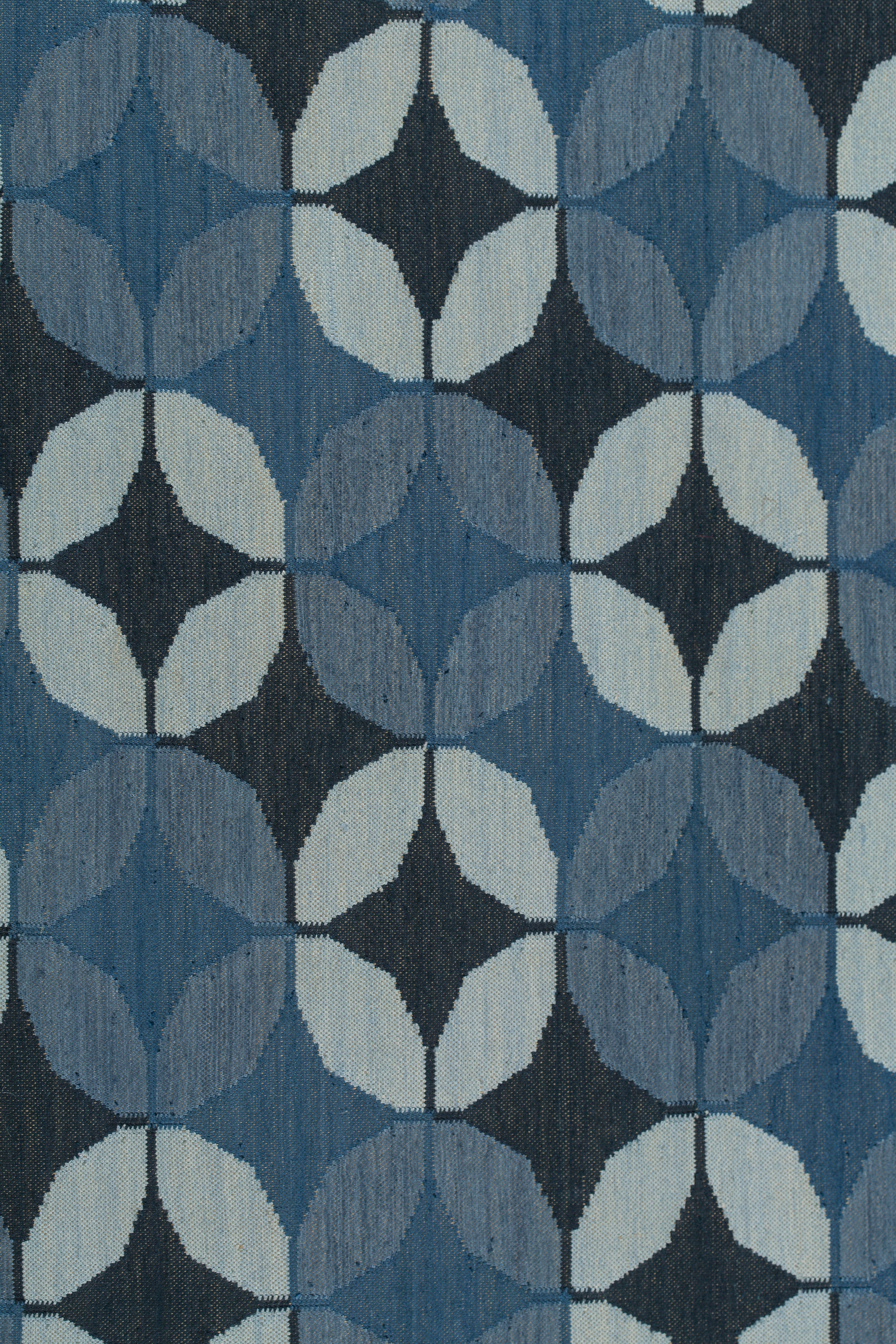 Detail of Alhambra Rug featuring a pattern of linked circles that create a star like lattice in a range of blue shades, from pale blue to chambray, indigo, to dark navy