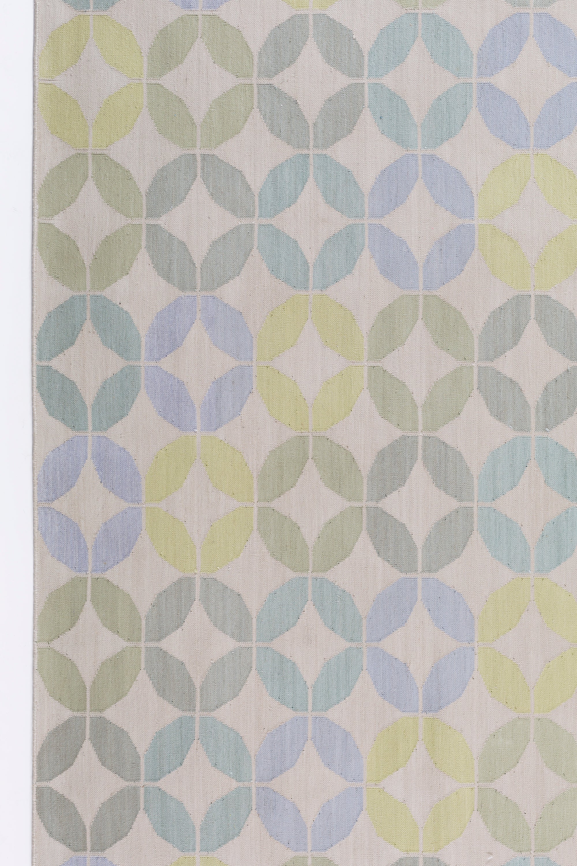 Detail of Alhambra Rug in Mint featuring a pattern of linked circles that create a star like lattice in a range of pastel turquoise, mint, yellow and lime green on a soft beige field. 