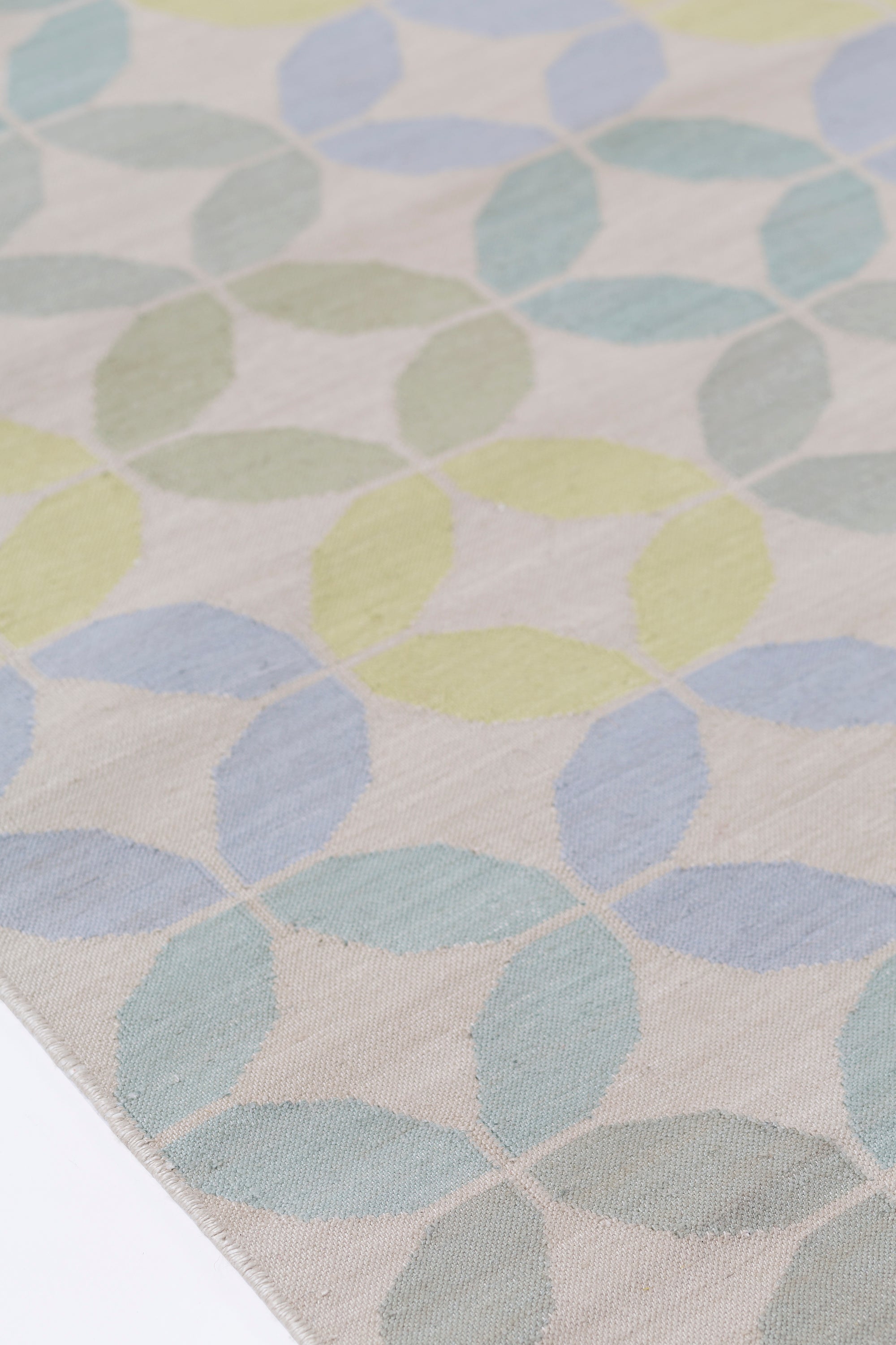 Detail of Alhambra Rug in Mint featuring a pattern of linked circles that create a star like lattice in a range of pastel turquoise, mint, yellow and lime green on a soft beige field. 