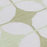 Detail of Alhambra Rug in Olive featuring pattern of linked circles that create a star like lattice in a soft olive and lime green on an ivory field. 