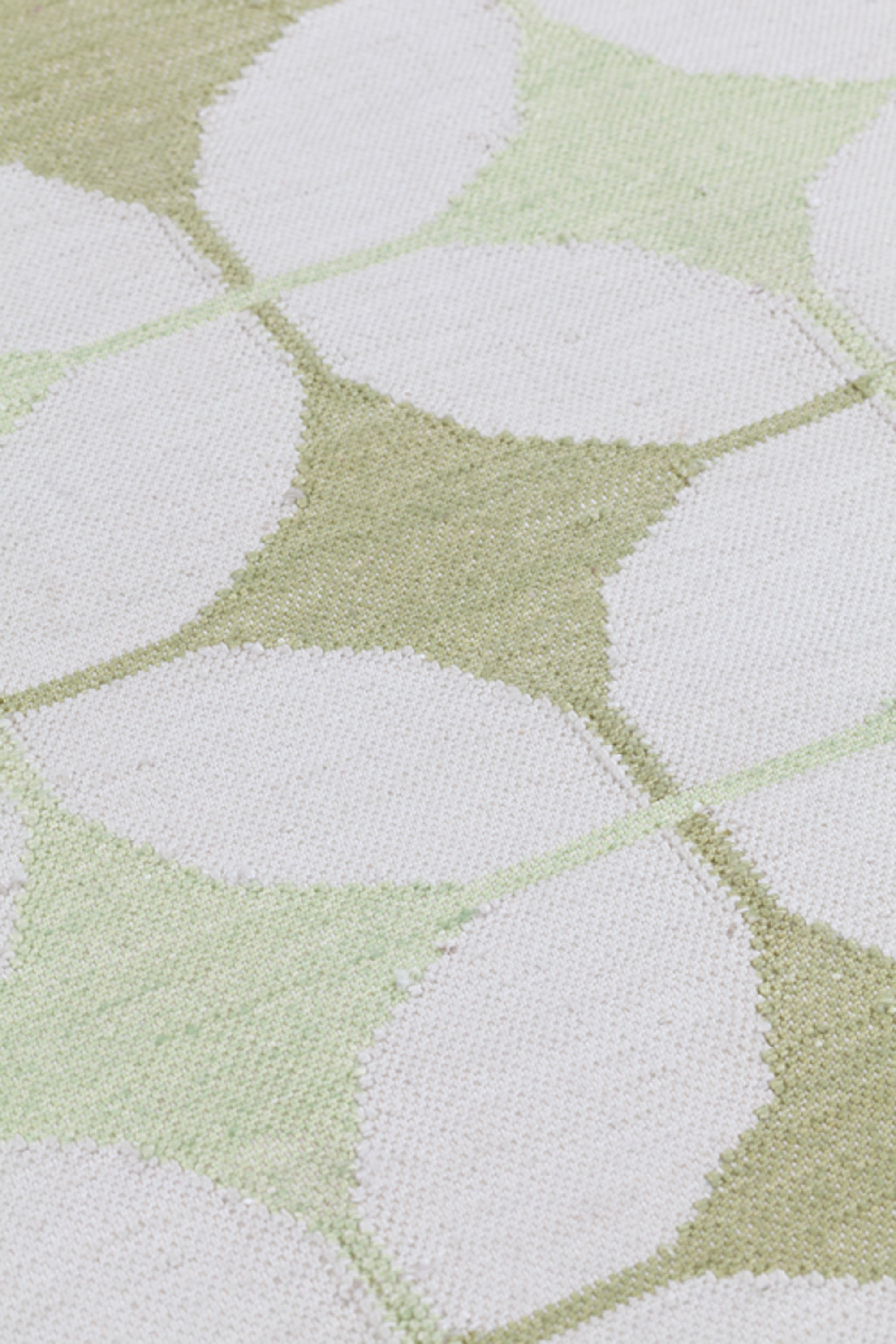 Detail of Alhambra Rug in Olive featuring pattern of linked circles that create a star like lattice in a soft olive and lime green on an ivory field. 