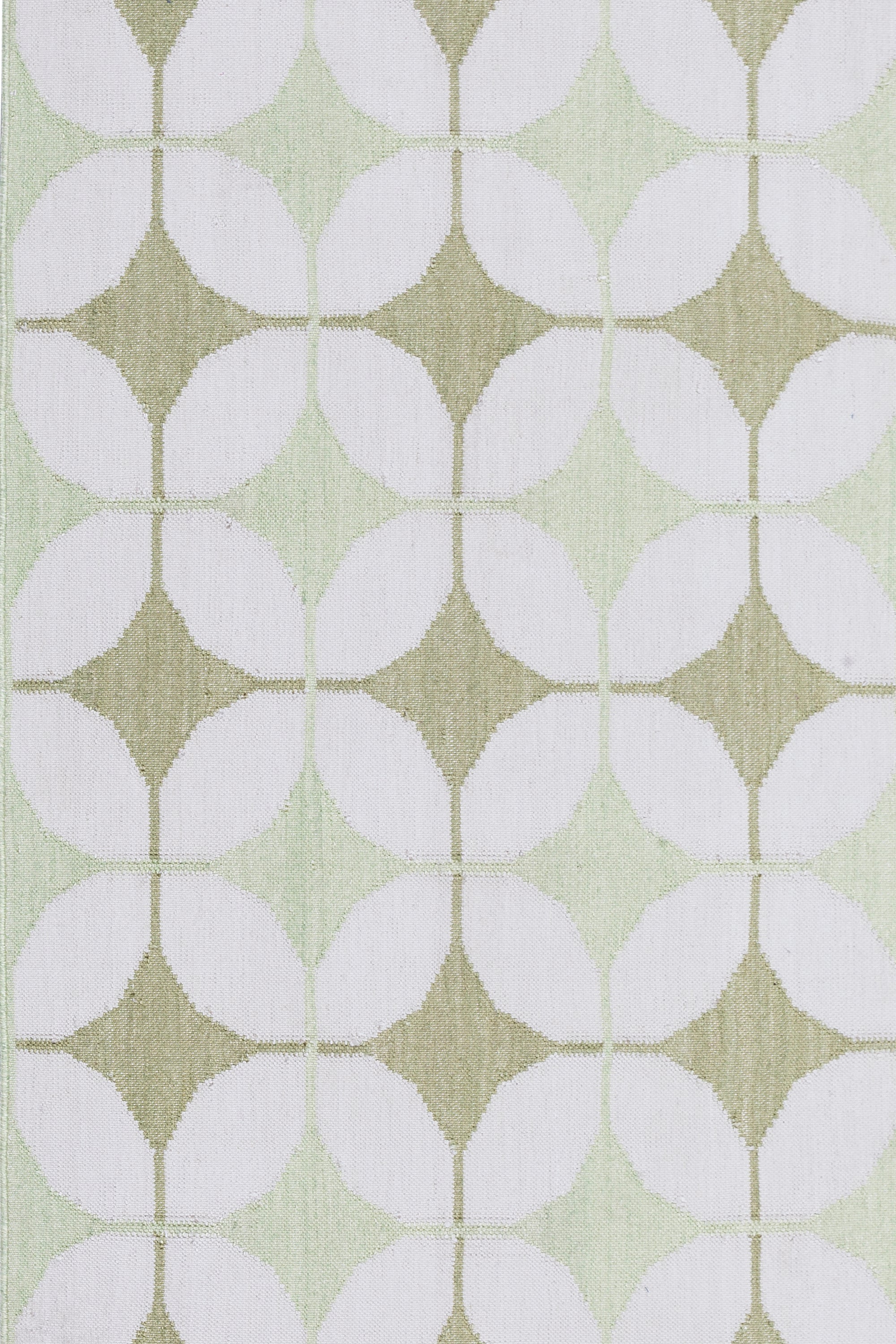 Detail of Alhambra Rug in Olive featuring pattern of linked circles that create a star like lattice in a soft olive and lime green on an ivory field. 