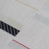 Detail of the Amelia Rug in Camara featuring a minimalist broken stripe pattern, overlayed with thin white diagonal lines. The broken stripes are a mix of black, pale blue and turquoise with accents of red and bright yellow, all on a soft grey field