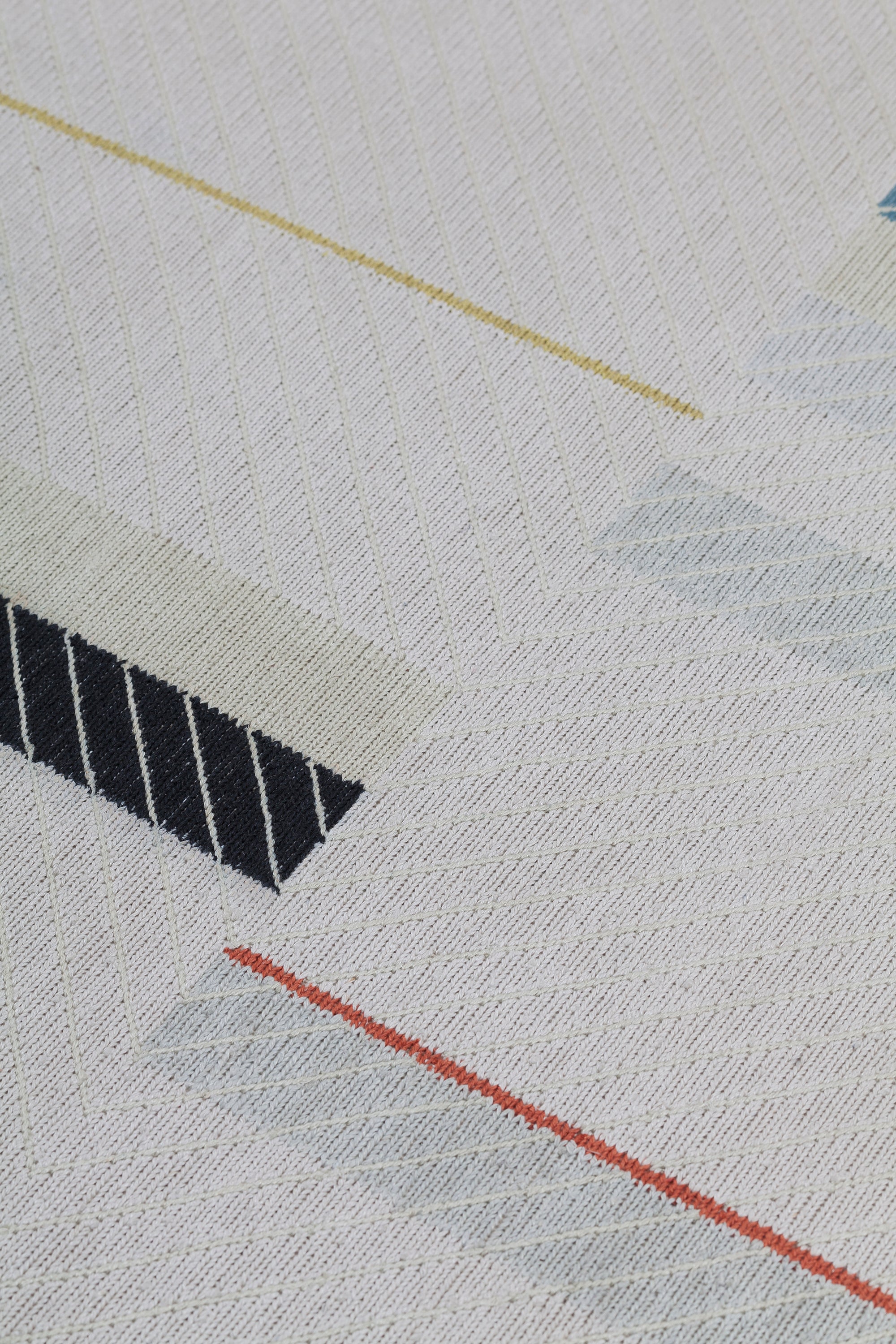 Detail of the Amelia Rug in Camara featuring a minimalist broken stripe pattern, overlayed with thin white diagonal lines. The broken stripes are a mix of black, pale blue and turquoise with accents of red and bright yellow, all on a soft grey field