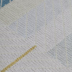 Detail of the Amelia Rug in Camara featuring a minimalist broken stripe pattern, overlayed with thin white diagonal lines. The broken stripes are a mix of black, pale blue and turquoise with accents of red and bright yellow, all on a soft grey field