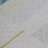 Detail of the Amelia Rug in Camara featuring a minimalist broken stripe pattern, overlayed with thin white diagonal lines. The broken stripes are a mix of black, pale blue and turquoise with accents of red and bright yellow, all on a soft grey field