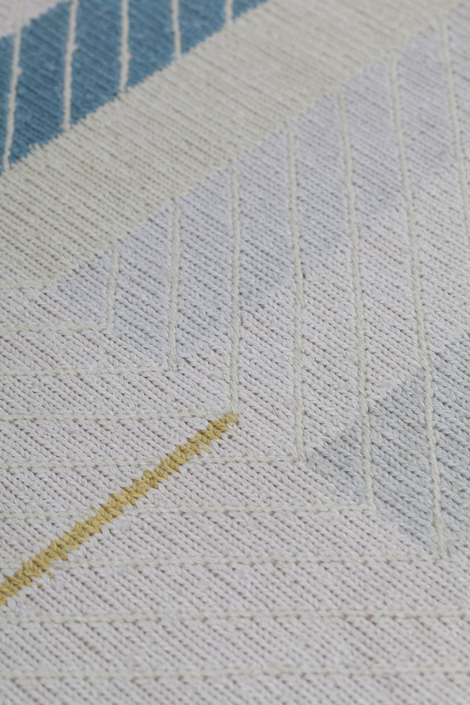 Detail of the Amelia Rug in Camara featuring a minimalist broken stripe pattern, overlayed with thin white diagonal lines. The broken stripes are a mix of black, pale blue and turquoise with accents of red and bright yellow, all on a soft grey field