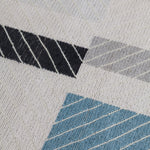 Detail of the Amelia Rug in Camara featuring a minimalist broken stripe pattern, overlayed with thin white diagonal lines. The broken stripes are a mix of black, pale blue and turquoise with accents of red and bright yellow, all on a soft grey field