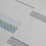 Detail of the Amelia Rug in Pearl featuring a minimalist broken stripe pattern, overlayed with thin white diagonal lines. The broken stripes are a mix of pale blues, grey, and turquoise with slate grey accents, all on a pale grey field. 