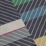 Detail of the Amelia Rug in Spinel featuring a minimalist broken stripe pattern, overlayed with thin black diagonal lines. The broken stripes are a mix of white, grey, kelly green, denim blue, black with hot pink accents, all on a charcoal grey field. 