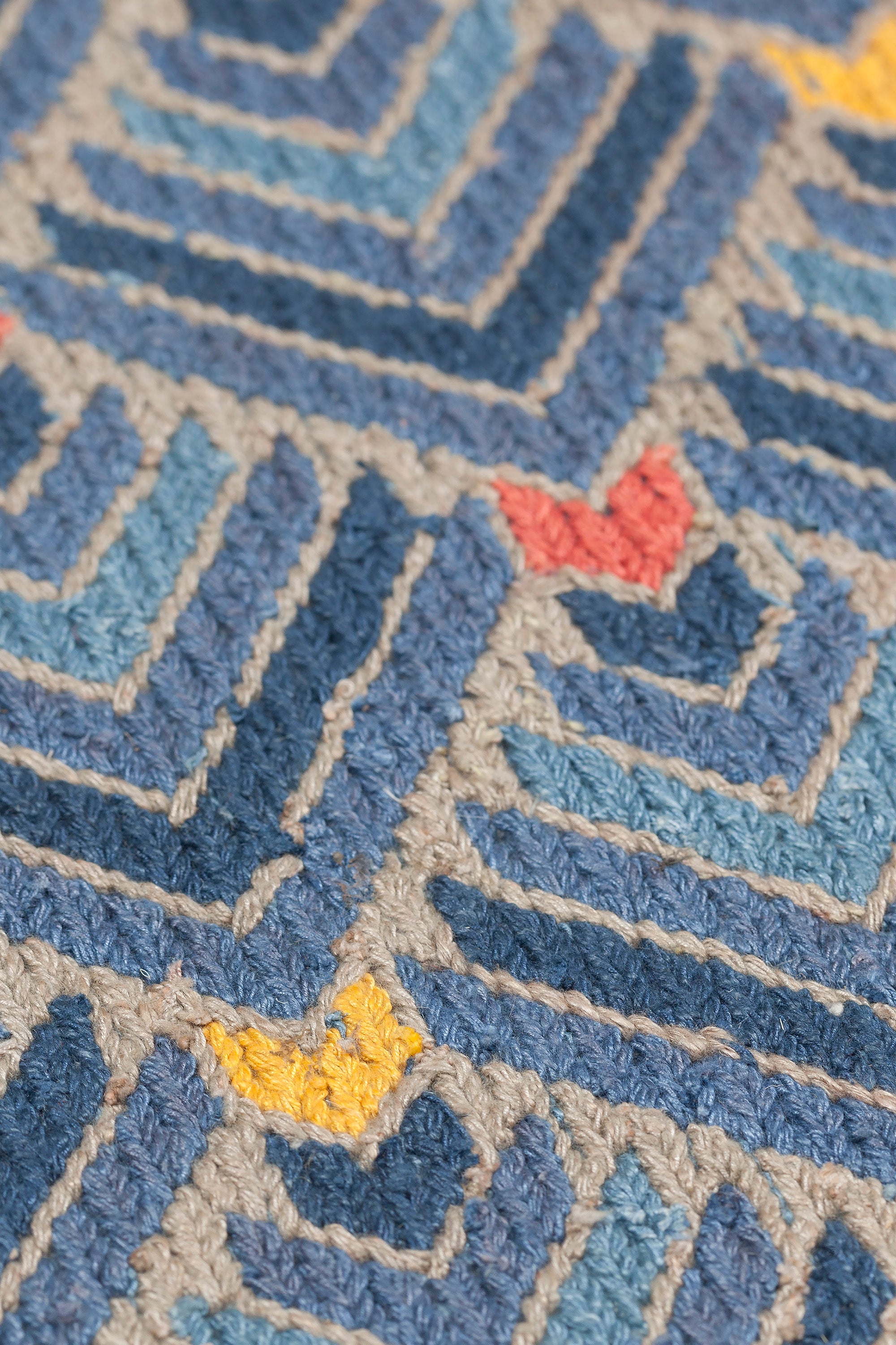 Detail of the Arrow Rug in Indigo-Coral features a dense pattern of nesting arrow shapes in shades of blue with accents of coral and yellow on a light brown field