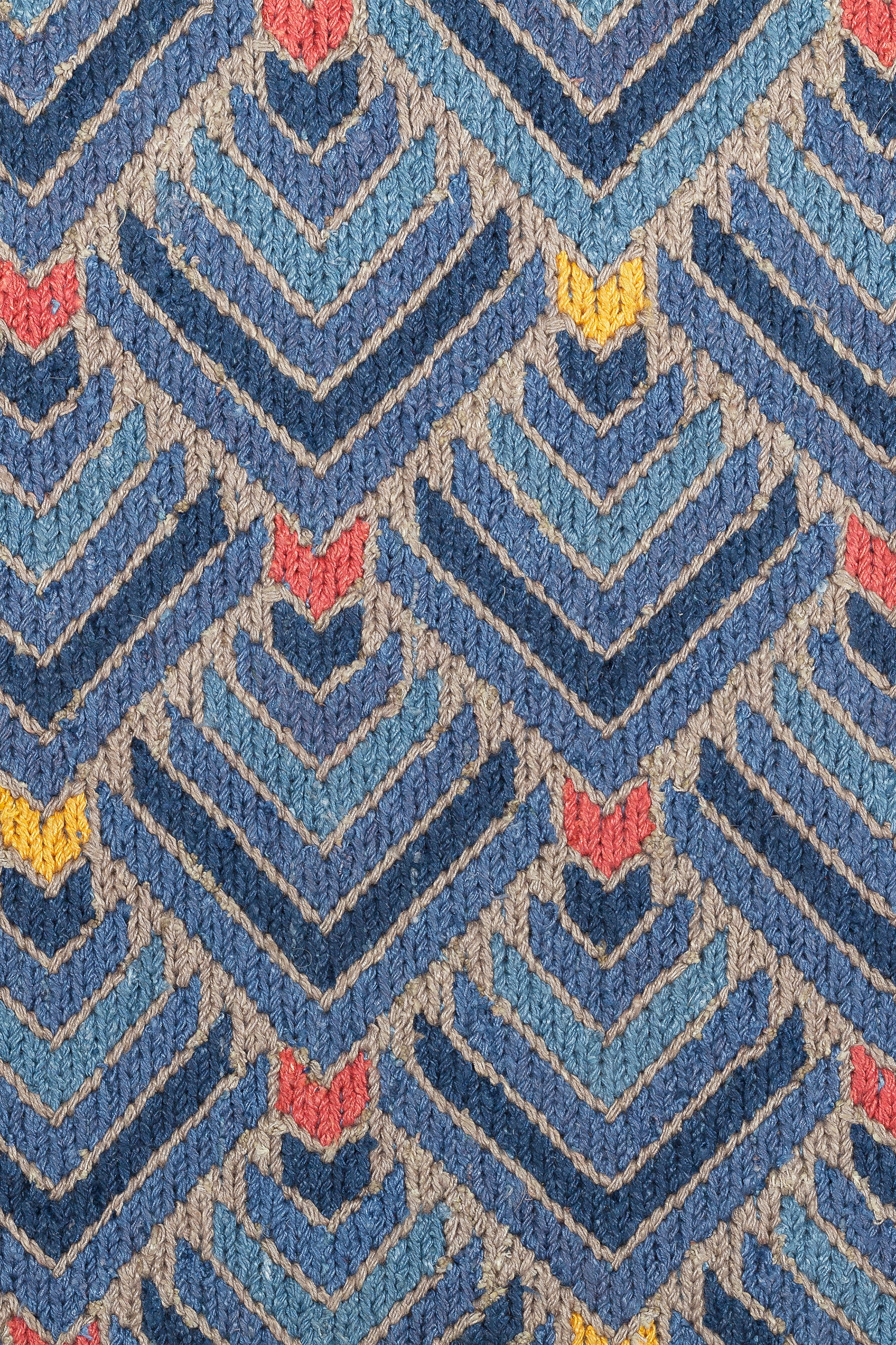 Detail of the Arrow Rug in Indigo-Coral features a dense pattern of nesting arrow shapes in shades of blue with accents of coral and yellow on a light brown field