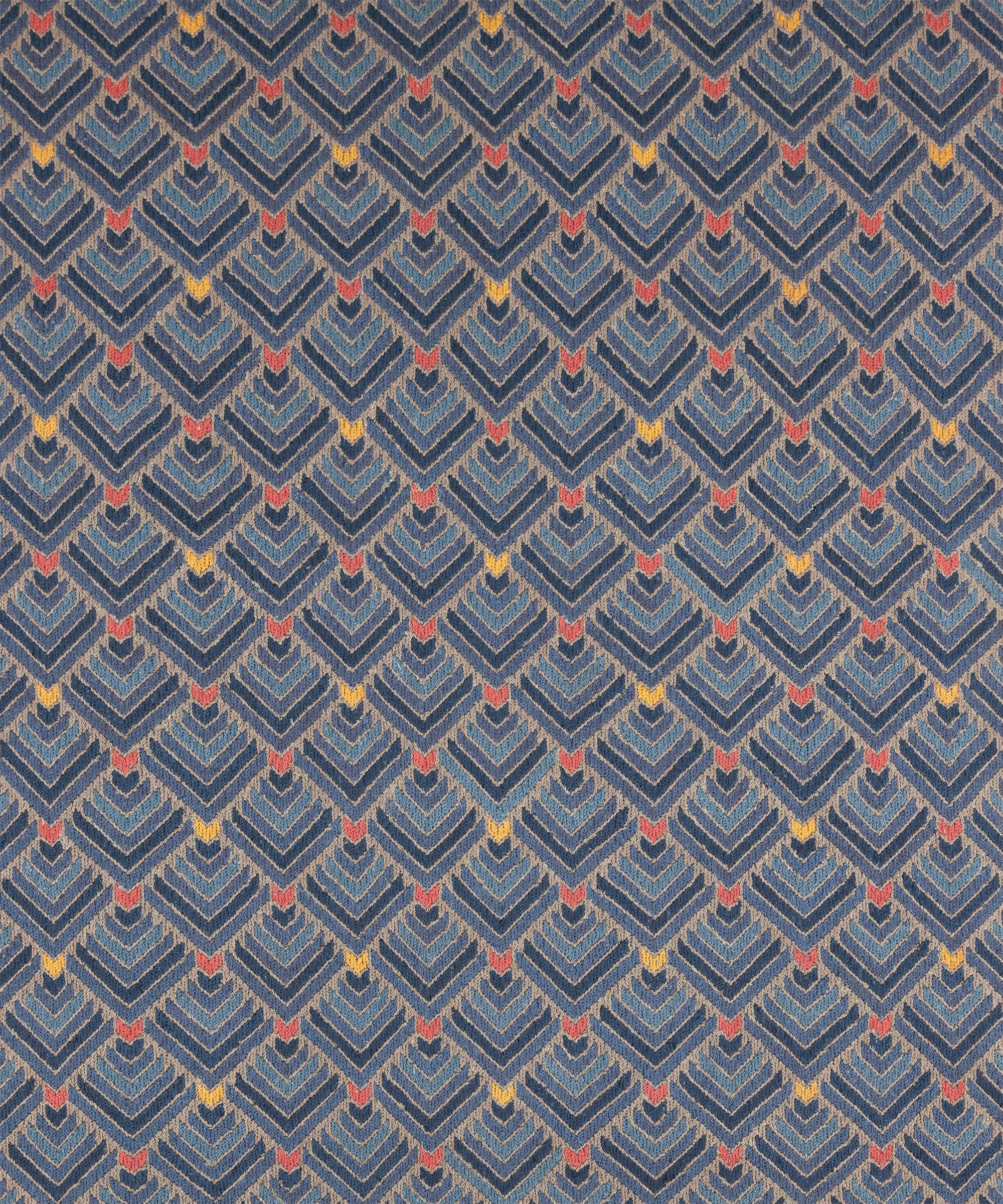 The Arrow Rug in Indigo-Coral features a dense pattern of nesting arrow shapes in shades of blue with accents of coral and yellow on a light brown field