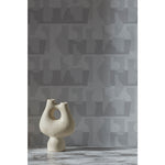 White vase in front of a wall with a pattern of pale grey geometric vessel shapes over a white background with soft grey horizontal stripes.