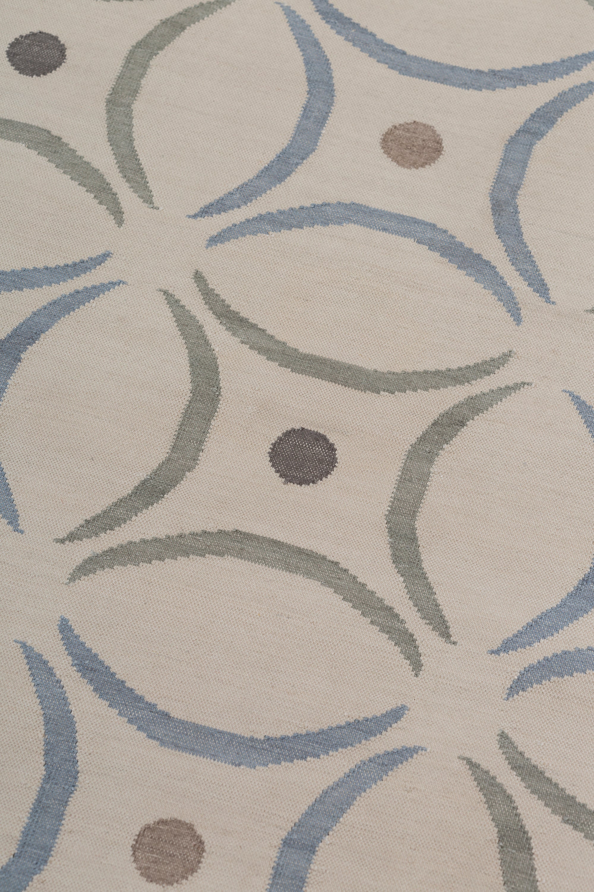 Detail of the Boe rug in Genoa, featuring a pattern of curved segments in light blue and sage green with taupe circles on an ivory field. 