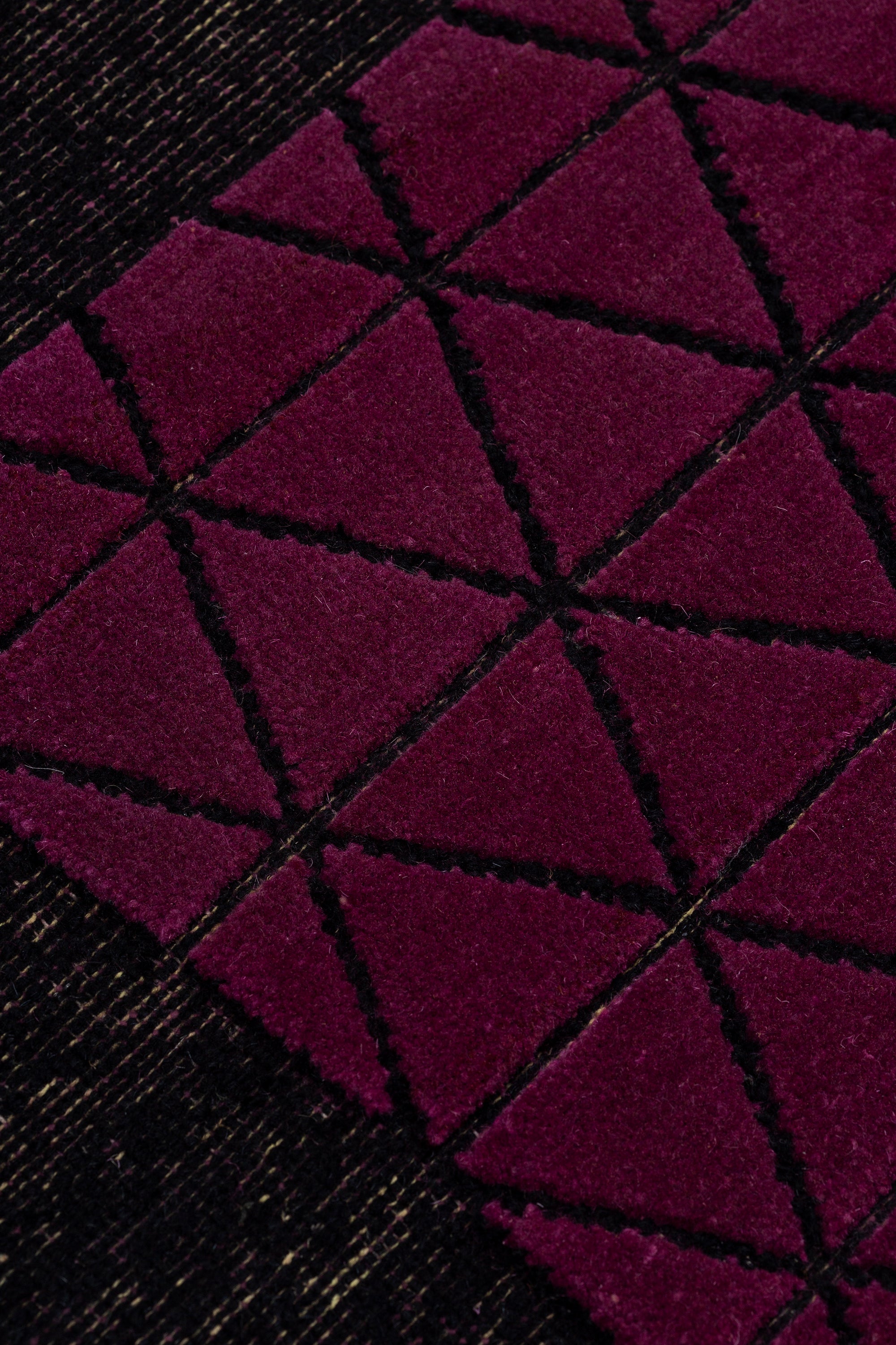 Detail of the Bucky Rug in berry, features a wide black border with a wine colored lattice field with a metallic sheen. 