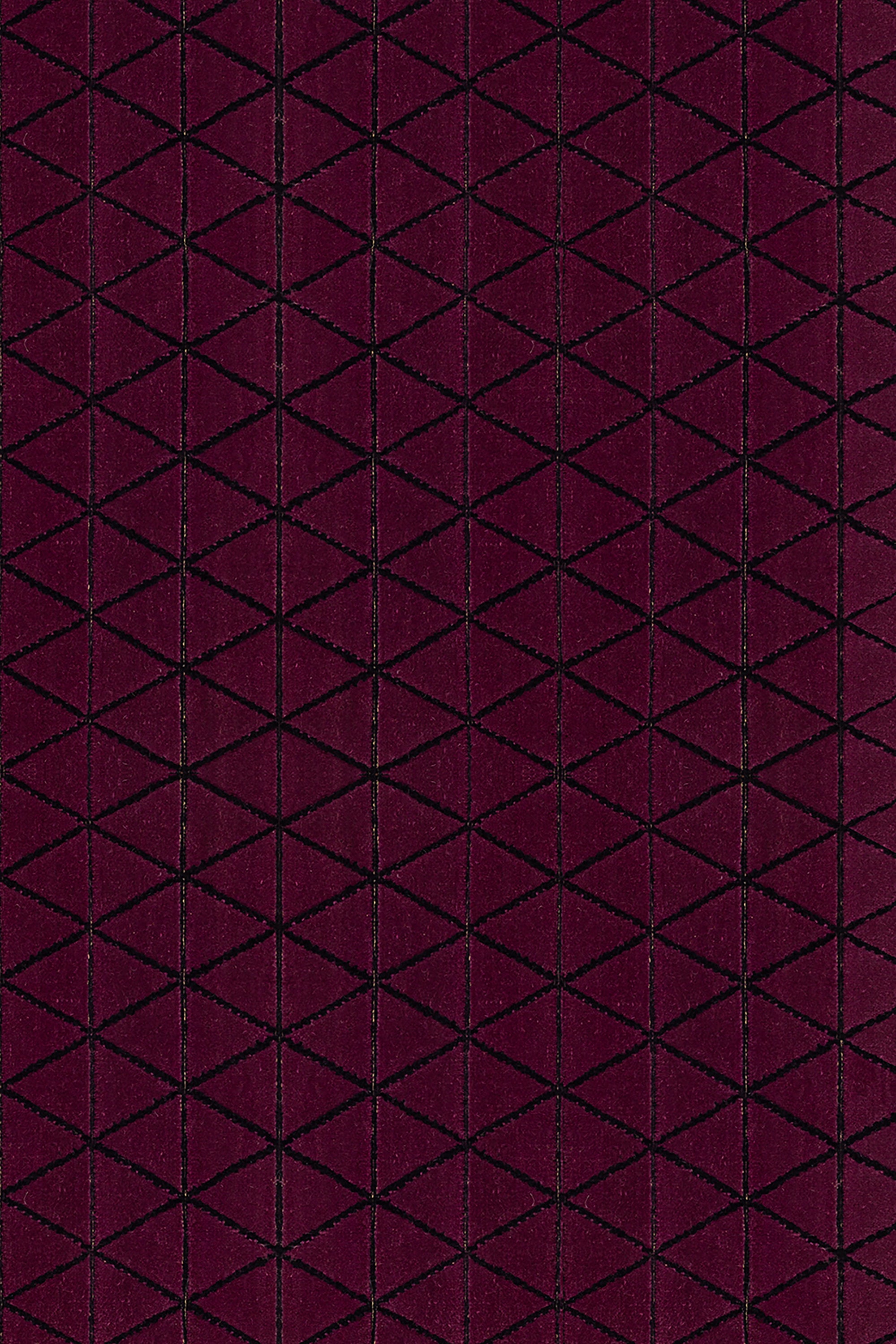 Detail of the Bucky Rug in berry, features a wide black border with a wine colored lattice field with a metallic sheen. 