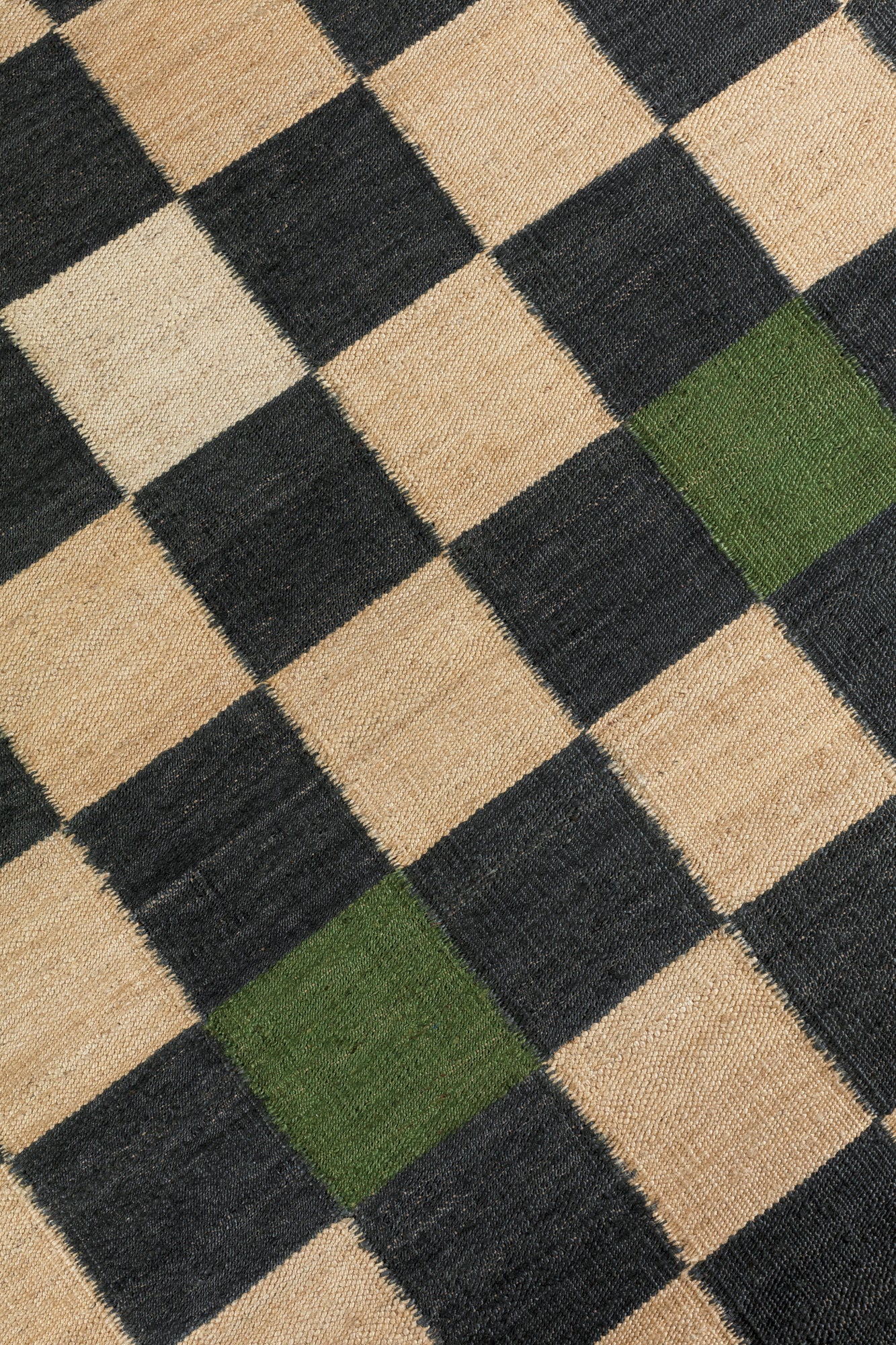 Detail of the Checkerboard Rug in King, a black and tan checkered pattern with random accents of green and white. 