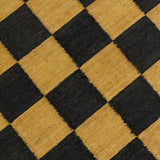 Detail of the Checkerboard Rug in Queen, a black and ochre yellow checkered pattern. 