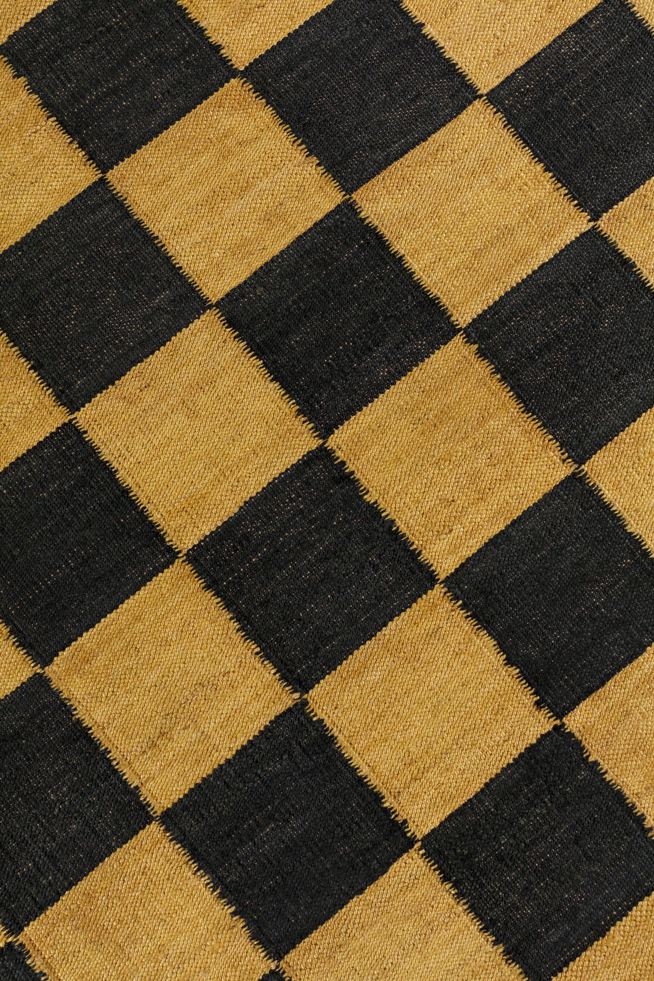 Detail of the Checkerboard Rug in Queen, a black and ochre yellow checkered pattern. 