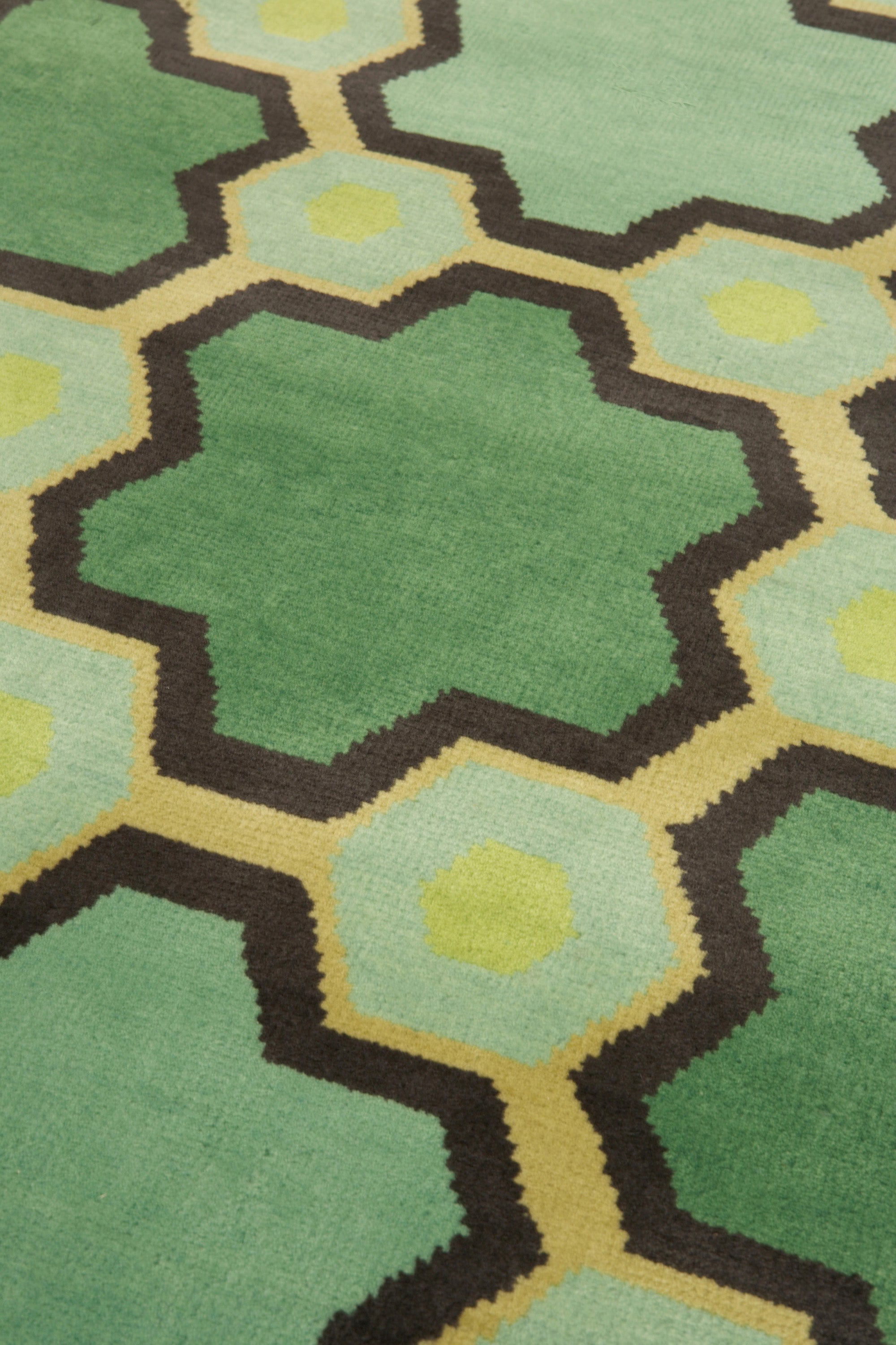 Detail of the Cordoba Cut Pile Rug in Emerald, a hexagonal lattice pattern with sahdes of emerald, jade, yelow and chcolate brown. 