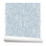 Partially unrolled wallpaper with a pattern of repeating watercolor illustrations of horses, farmers and country houses in white on a blue background.