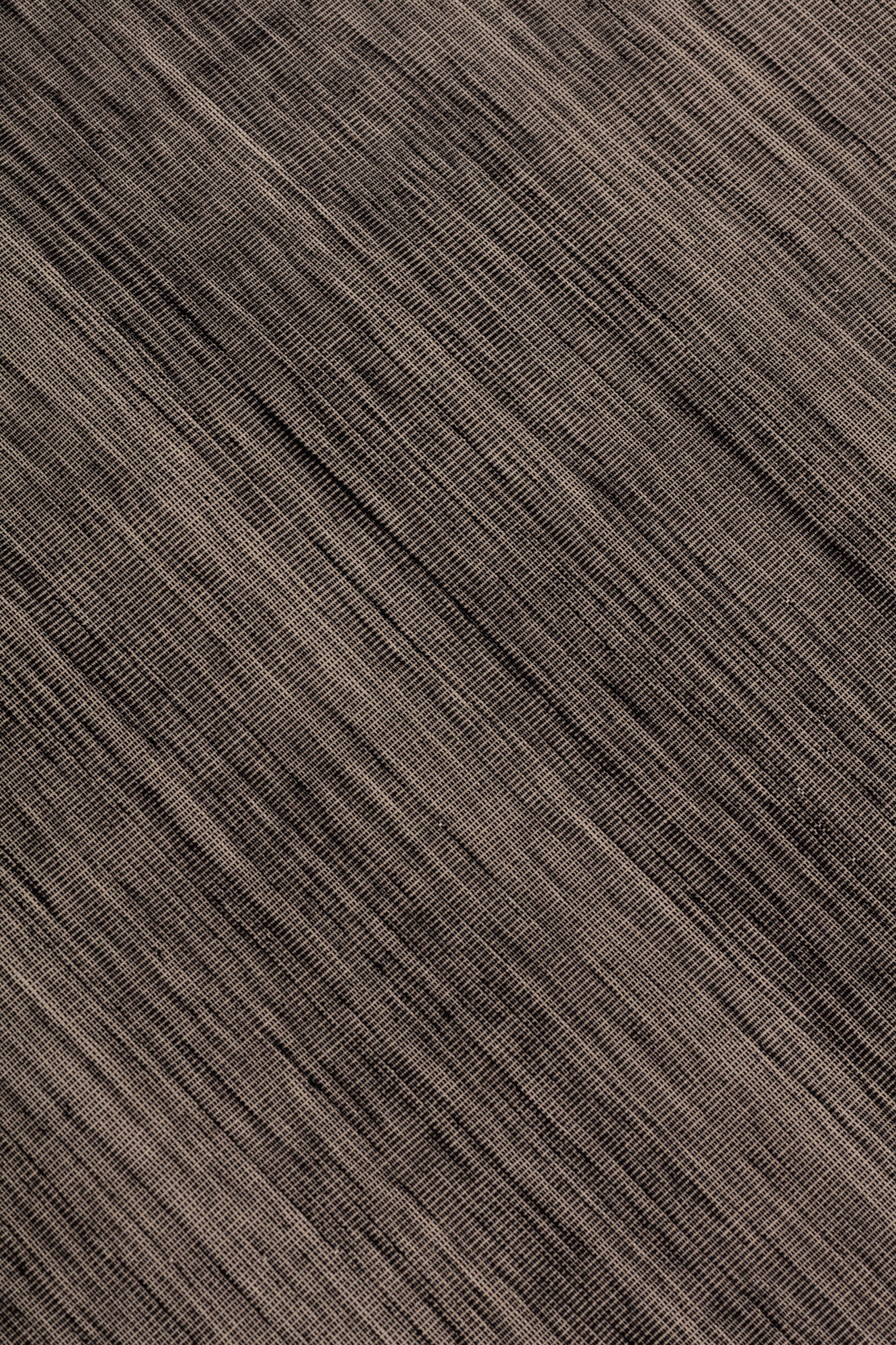 Detail of the Moire Rug in Rockpool, a subtle striated pattern tan and black. 