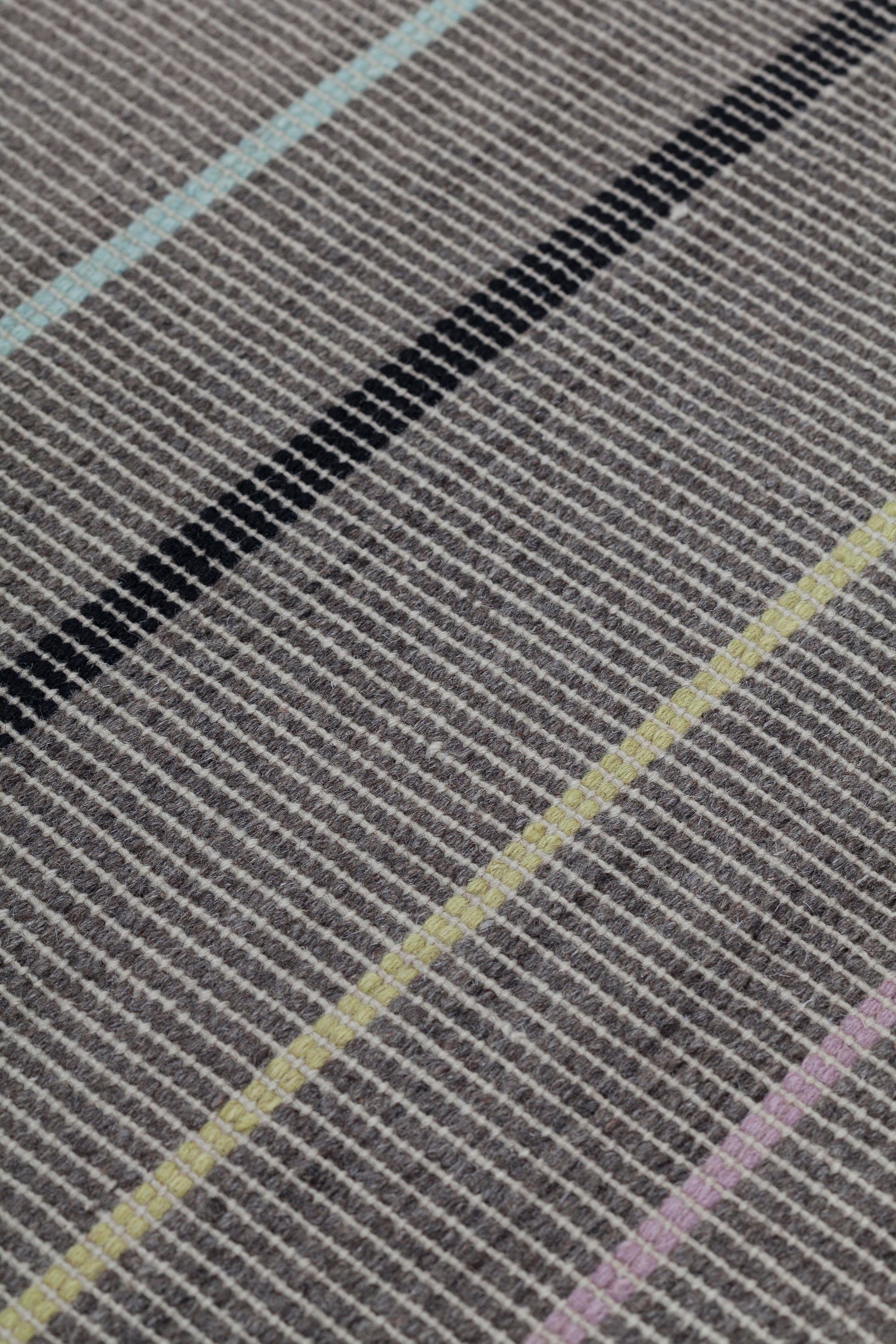 Detail of the Jasper Waffle Rug in Jet, widely spaced thin stripes of yellow, pink, black, acqua and white on a grey field. 