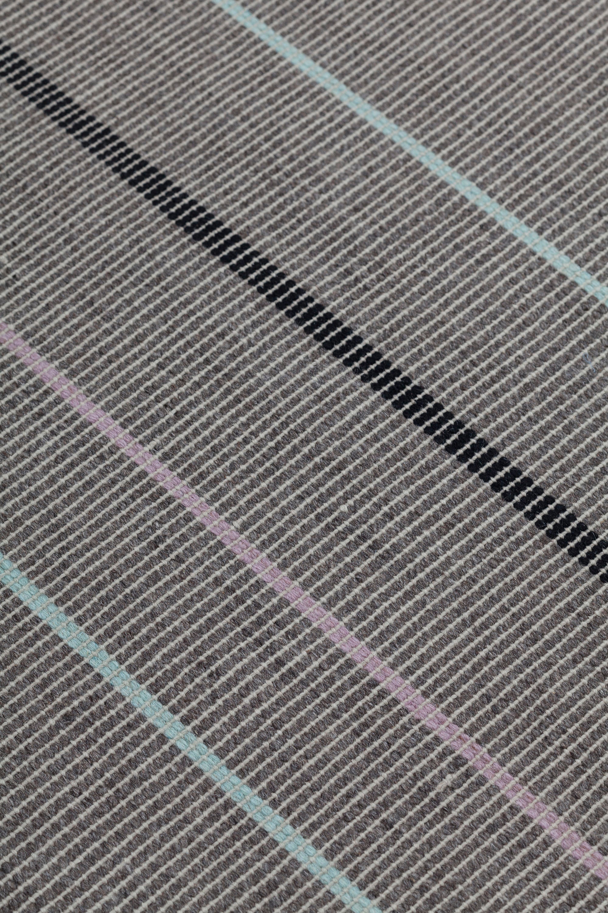 Detail of the Jasper Waffle Rug in Jet, widely spaced thin stripes of yellow, pink, black, acqua and white on a grey field. 
