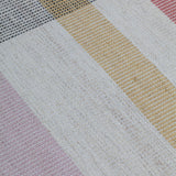 Detail of the Jasper Waffle Rug in Red Fossile, widely spaced stripes of yellow, pink, red, white and black on a split light grey fand ivory field. 