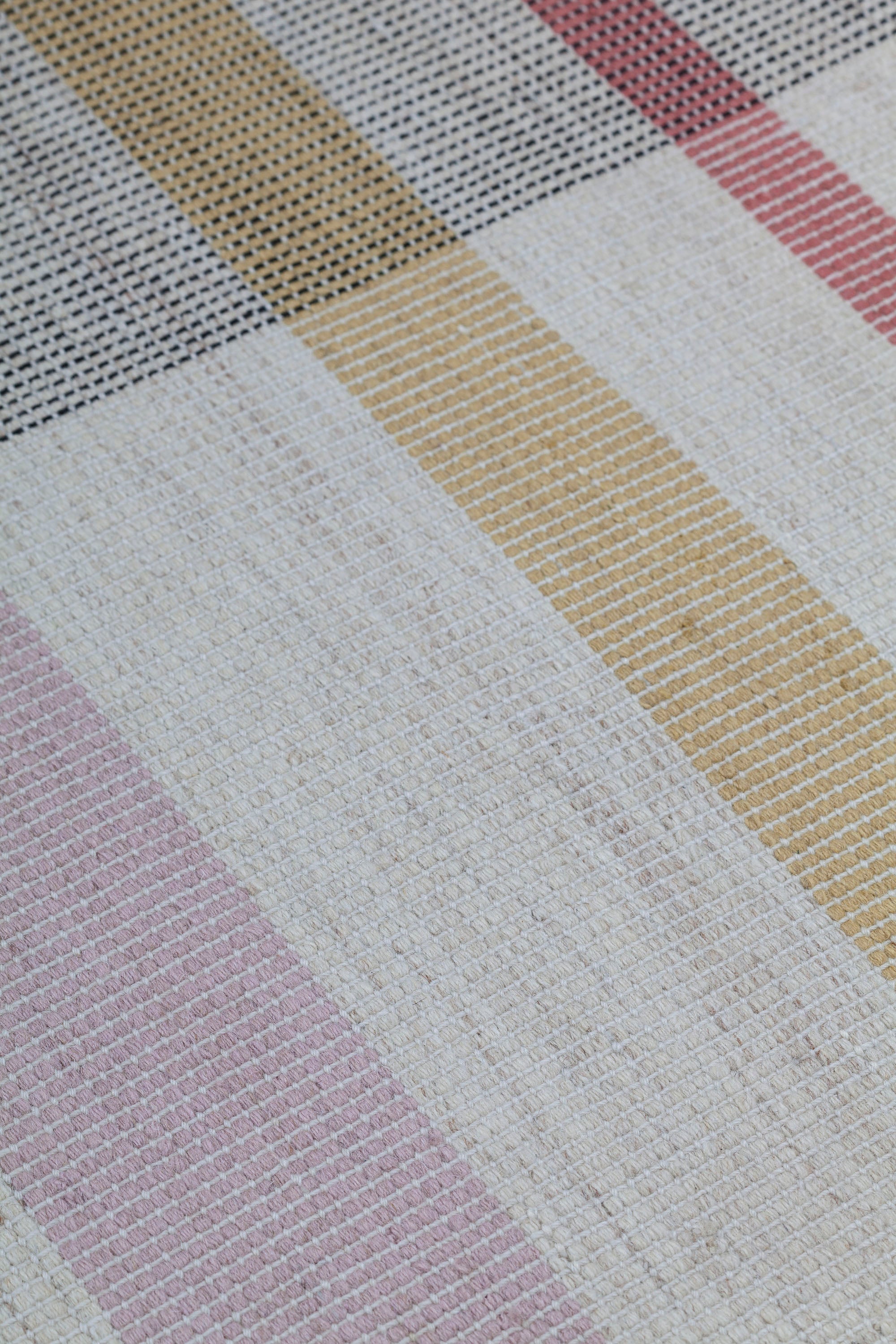 Detail of the Jasper Waffle Rug in Red Fossile, widely spaced stripes of yellow, pink, red, white and black on a split light grey fand ivory field. 