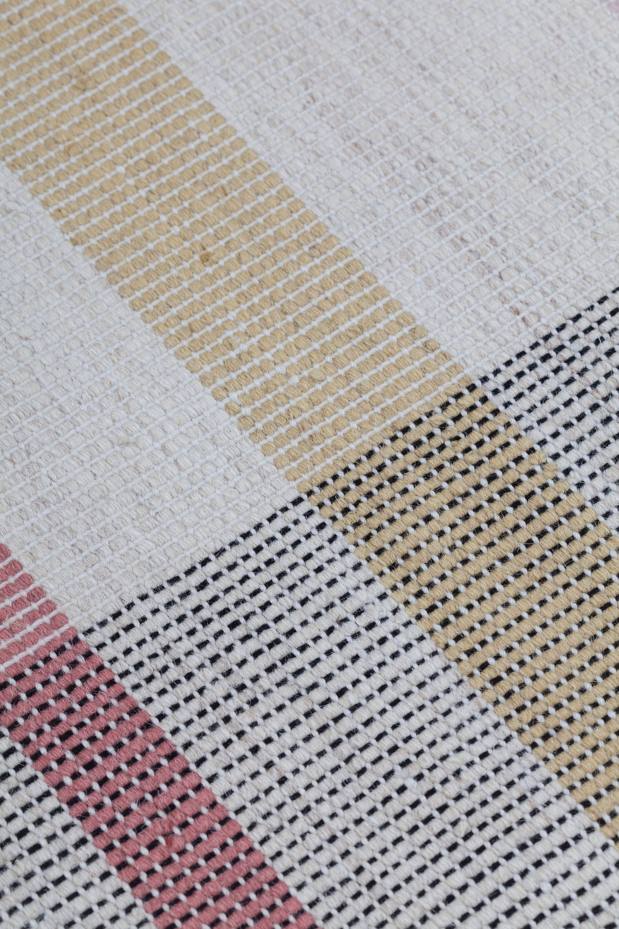 Detail of the Jasper Waffle Rug in Red Fossile, widely spaced stripes of yellow, pink, red, white and black on a split light grey fand ivory field. 